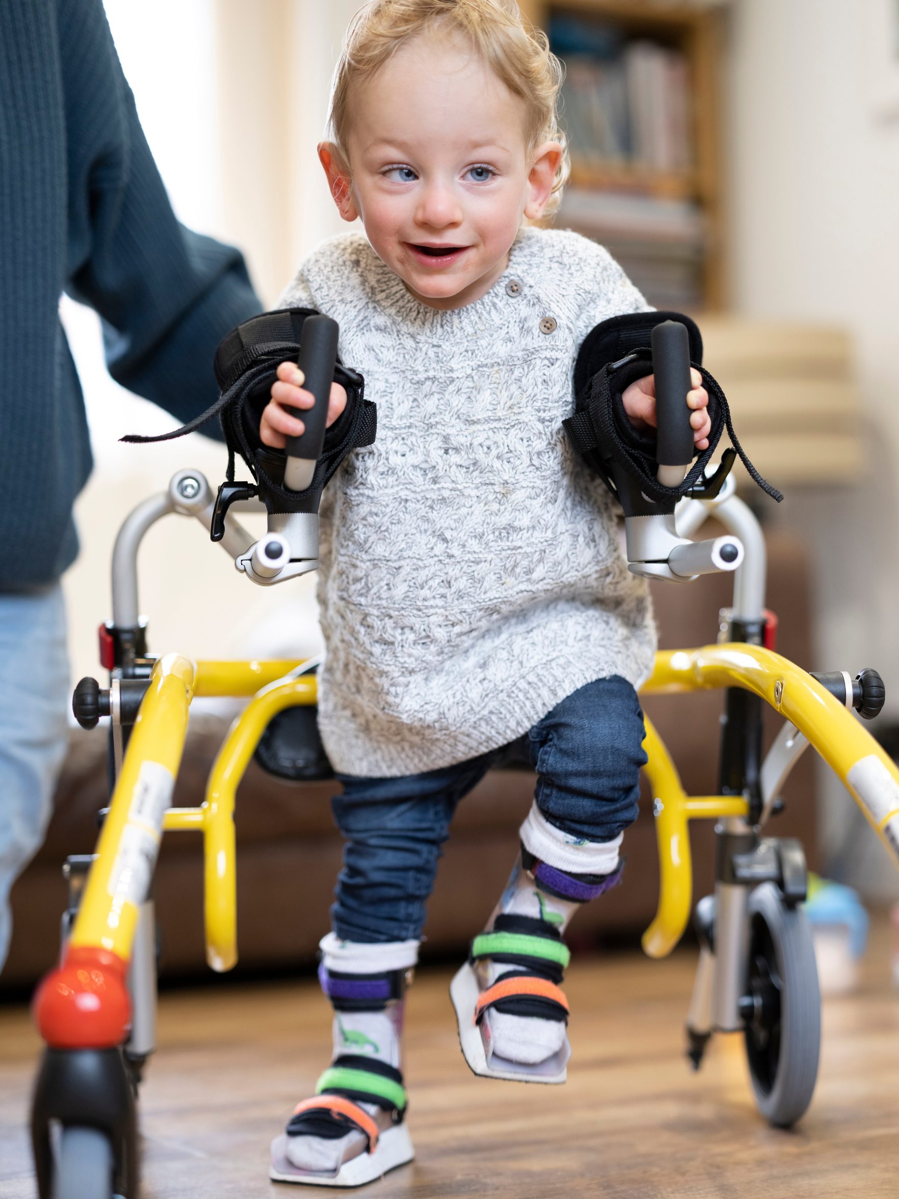 Liikumispuudega laps käimisraamiga hoiab täiskasvanul käest kinni.