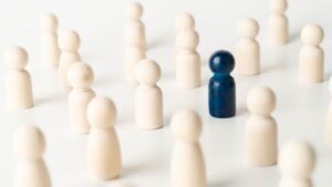 Heledal taustal rühm puidust lauamängu kujukesi, mis on heledat puiduvärvi. Üks neist on tumesinine.