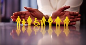 Pildil on reas kollased inimfiguurid, sh ratastoolikasutaja ja erinevas vanuses inimesed, ning nende kohal hoiab keegi käsi kaitsvasse asendisse. Kujund viitab sotsiaalsele kaitsele, hoolivusele ja kaasamisele.