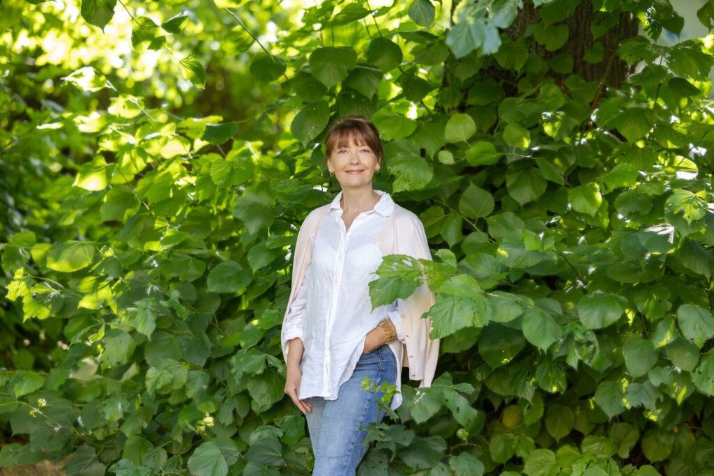 EPIKoja tervishoiualase huvikaitse nõunik Tuuli Seinberg valge särgi ja teksapükstega roheliste puude taustal.