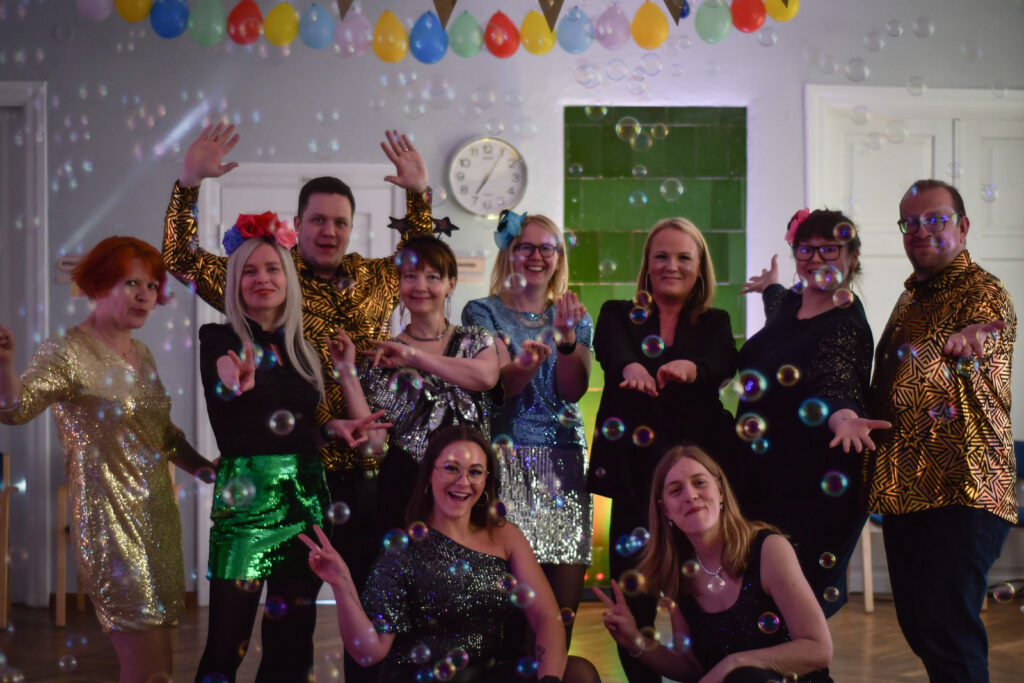 EPIKoja tiim ühiselt fotol suures saalis, kokku 10 inimest. Kõigil on seljas sädelevad ja helkivad riided, mis sobivad diskole. Fotol on lastud tossumasinaga tossu ning mullimasinaga mulle. Ruum on õhupallidega kaunistatud.