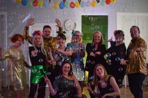 EPIKoja tiim ühiselt fotol suures saalis, kokku 10 inimest. Kõigil on seljas sädelevad ja helkivad riided, mis sobivad diskole. Fotol on lastud tossumasinaga tossu ning mullimasinaga mulle. Ruum on õhupallidega kaunistatud.