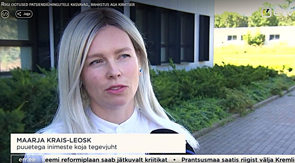 Heledapäine naisterahvas (EPIKoja tegevjuht Maarja Krais-Leosk) andmas intervjuud. Tema ees ERR mikrofon ja taustal rohelus ja mustade aknaraamidega hele maja