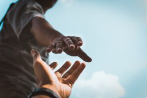 Kaks kätt sirutuvad üksteise poole sinise taeva taustal, üleval käsi ulatub alla, all käsi ulatub üles abi vastu võtma.